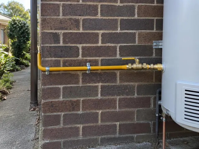 Yellow gas pipe with valve on a brick wall beside a water heater in Bellevue Hill